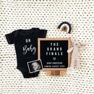 May include: A black onesie with the text "Oh Baby" in white lettering, a black letter board with the text "The Grand Finale" and a heart, a black and white ultrasound image, and wooden blocks spelling "Baby".