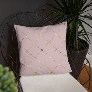 May include: A pink cushion with a gold geometric pattern. The cushion is sitting on a black metal chair.