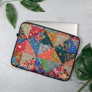 May include: A colorful laptop sleeve with a patchwork design featuring various floral patterns and geometric shapes. The sleeve is made of a durable fabric and has a zipper closure.