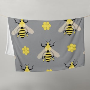May include: A gray fabric with a repeating pattern of yellow bees and honeycombs. The bees are cartoon-style and have black eyes and wings.