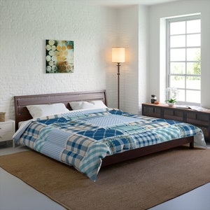 Op de afbeelding: Een blauwe en witte geruite dekbedovertrek met een patchwork-ontwerp. De dekbedovertrek ligt op een bed met een houten hoofdeinde en een bruin tapijt.