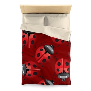 Könnte beinhalten: Eine rote Bettdeckenbezug mit einem sich wiederholenden Muster aus Cartoon-Marienkäfern mit schwarzen Punkten. Die Marienkäfer haben schwarze Köpfe und Fühler. Die Bettwäsche befindet sich auf einem Bett mit einem hellen Holz-Kopfteil und weißen Kissen.