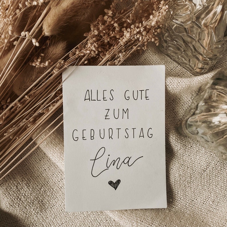 Puede incluir: Una tarjeta blanca con texto escrito a mano en negro que dice "Alles Gute zum Geburtstag Lina" con un peque&ntilde;o coraz&oacute;n negro debajo del nombre.
