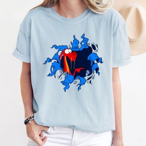 May include: A light blue t-shirt with a cartoon image of a red dragon bursting out of a blue and white comic book style frame. The dragon has a surprised expression and is holding a small blue object.