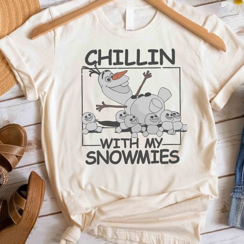 May include: A white t-shirt with a cartoon image of Olaf from Frozen. Olaf is surrounded by smaller snowmen. The text "Chillin' with my snowmies" is printed on the shirt.
