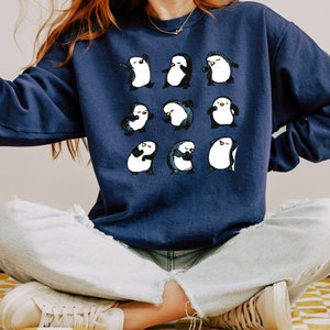 May include: A navy blue sweatshirt with a graphic of 12 penguins dancing. The penguins are white with black accents and are arranged in a grid pattern.