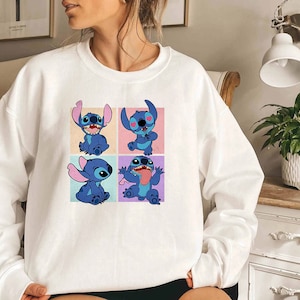 May include: White sweatshirt featuring a colorful graphic of the character Stitch from the animated film Lilo & Stitch. The design showcases Stitch in four different poses, each set against a pastel background. A comfortable, casual top.
