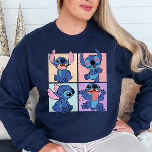 May include: Navy blue sweatshirt featuring a four-panel graphic of the character Stitch from Lilo & Stitch. Each panel shows Stitch in a different pose, with a variety of expressions. The sweatshirt is a solid color, with a crew neck.