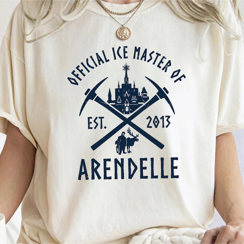 May include: A white t-shirt with a blue graphic design. The graphic features a castle, crossed pickaxes, and the text "Official Ice Master of Arendelle Est. 2013".