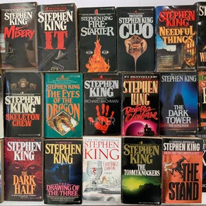 以下が含まれることがあります： 様々な表紙デザインの、スティーブン・キングの書籍コレクション。「デッドゾーン」、「ミザリー」、「IT」、「ファイアスターター」、「クーヨ」、「ニードフル・シングス」、「ザ・ウェイストランズ」などのタイトルが含まれています。本は列に並べられ、さまざまな色とイラストが展示されています。