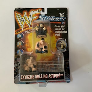 Puede incluir: Un juego de juguetes WWF Sliders con tres figuras de lucha libre en un paquete de plástico transparente. El embalaje incluye el logotipo de la WWF, el texto "Sliders" y "Extreme Rolling Action!". El juego incluye tres objetivos.