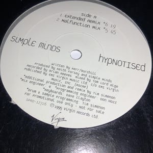 Peut inclure: Un disque vinyle noir avec une étiquette blanche portant le nom du groupe "SIMPLE MINDS" et le titre "HYPNOTISED". L'étiquette comprend les titres des chansons, les crédits et le logo Virgin Records. Le disque est destiné à un usage promotionnel.