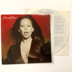 May include: A vintage vinyl record album titled "Night Flight" by Yvonne Elliman. The album cover features a portrait of the artist with long dark hair against a red background. The record sleeve is visible.