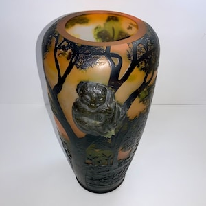 May include: A tall, amber-coloured glass vase with a frosted finish. The vase features a detailed, black silhouette of a monkey sitting in a tree, surrounded by other trees and foliage.
