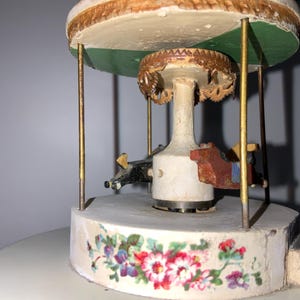 May include: A vintage wooden carousel with painted details, featuring a green roof, a white base with floral designs, and a central rotating platform with wooden horses.