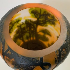 May include: A large, round, dark grey and orange glass vase with a textured exterior. The inside of the vase is painted with a light orange, yellow, and green landscape scene.