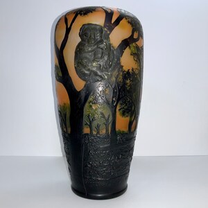May include: A black and amber glass vase with an embossed design of a koala bear in a tree. The vase has a textured surface and a rounded shape.