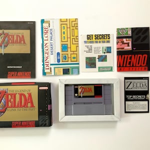Puede incluir: Colección de artículos de videojuegos vintage de "The Legend of Zelda: A Link to the Past" para Super Nintendo. Incluye caja del juego, cartucho, manual de instrucciones y guías. La caja presenta el logotipo del juego con una espada.