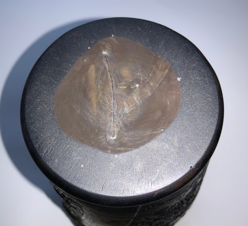 May include: A black ceramic vase with a textured surface and a brown circular patch on the top.