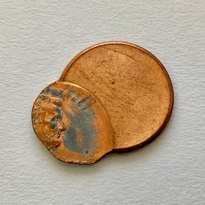 Op de afbeelding: Een koperen cent met een gedeeltelijke afbeelding van Abraham Lincoln op de voorzijde. De cent is doormidden gevouwen, waardoor de achterzijde van de munt zichtbaar is.