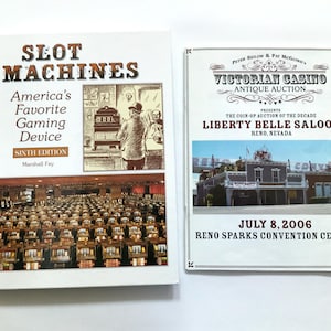 May include: Two books about slot machines. The book on the left is titled "Slot Machines: America's Favorite Gaming Device" and is the sixth edition by Marshall Fey. The book on the right is an advertisement for a Victorian Casino Antique Auction, featuring the Liberty Belle Saloon in Reno, Nevada. The auction is scheduled for July 8, 2006, at the Reno Sparks Convention Center.