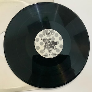 May include: A black vinyl record with a white and grey label featuring a cartoon figure and the text "Vibe". The label is surrounded by grey polka dots. The record is in a white sleeve.