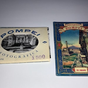 May include: Two vintage souvenir photo albums from Pompeii. One album is cream-colored with the word "Pompei" and "Fotografica" printed on it. The other album is blue with a colorful image of Pompeii ruins and the words "Ricordo di Pompei".