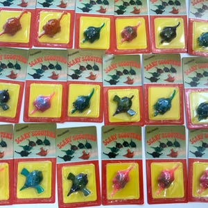 May include: A collection of twenty individual blister packs, each containing a single small plastic toy creature labeled Scary Scooters. The toys are molded in various colors including red, green, blue, and black, and are sealed under clear plastic bubbles on rectangular cardboard backing cards.
