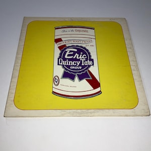 May include: Vintage album cover featuring a stylized beer can design with the text "This is the ORIGINAL" and "DRINKING MANS FRIEND". The can has a purple ribbon with "Eric Quincy Tate GROUP" and a star emblem. The background is yellow.