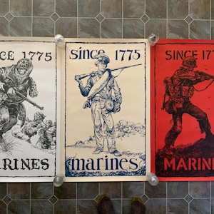 May include: Three vintage posters with the text "Since 1775 Marines" in blue and white lettering. The posters feature black and white illustrations of Marines in different poses. The left poster has a white background, the middle poster has a cream background, and the right poster has a red background.