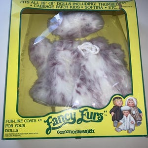 May include: A box of Fancy Furs fur-like coats for 16-18 inch dolls. The box features a white and purple fur coat with a white fur hat. The text on the box reads "Fancy Furs" and "commonwealth".