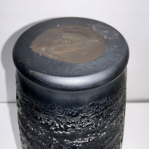 May include: Black ceramic vase with a textured surface. The top of the vase has a smooth, dark brown finish.