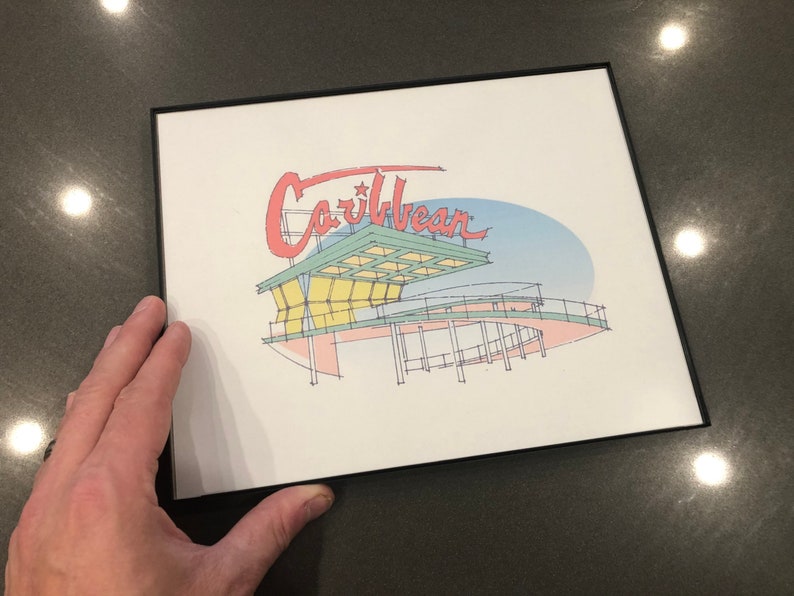May include: A framed print of a stylized illustration of a building with the word "Caribbean" in red lettering above it. The building is drawn in a light blue, green, and yellow color scheme.