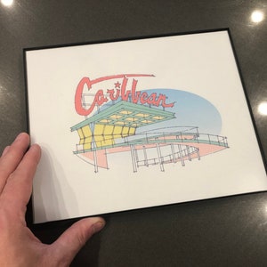 May include: A framed print of a stylized illustration of a building with the word "Caribbean" in red lettering above it. The building is drawn in a light blue, green, and yellow color scheme.