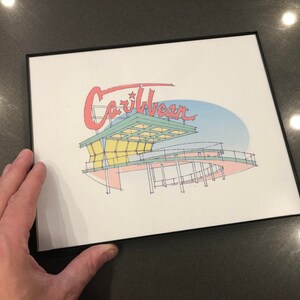 May include: A framed print of a stylized illustration of a building with the word "Caribbean" in red lettering above it. The building is drawn in a light blue, green, and yellow color scheme.