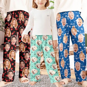 May include: Three pairs of pajama pants with custom face prints. One pair is black with red hearts and smiling faces. Another is teal with dog faces and paw prints. The third is blue with baby faces and white stars.