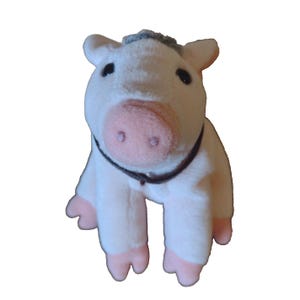 May include: A plush pig toy with a light pink body, a pink snout, and black eyes. The pig has a dark brown collar and gray hair on top of its head. The pig's hooves are also pink.
