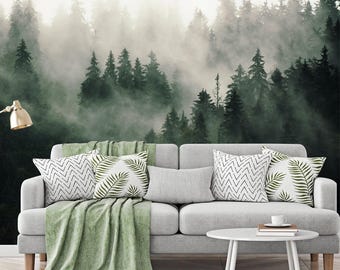 May include: A grey sofa with patterned cushions and a green throw. The cushions feature white and black geometric and leaf designs. A white coffee table holds a book and a cup. The backdrop is a misty forest scene.