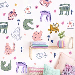 May include: A white wall adorned with whimsical cat illustrations in diverse colours and patterns. The cats feature pink, green, yellow, and purple hues, with floral and striped designs. Small pink flowers, blue hearts, and palm tree illustrations are also present.