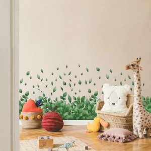 May include: A nursery room decorated with a green leafy wall decal. The room features a wicker chair with a white plush pillow, a giraffe stuffed animal, and a yellow duck toy. There are also two red and yellow apple-shaped baskets.