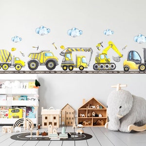 Watercolor construction vehicles wall decals arranged above a shelf in a modern nursery with toys and books