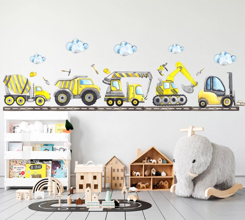 Watercolor construction vehicles wall decals arranged above a shelf in a modern nursery with toys and books