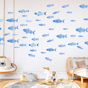 Pode incluir: Uma parede branca com adesivos de peixes de aquarela azul. Os peixes são de vários tamanhos e estão dispostos em formação de cardume. Há um cavalo de balanço de madeira e um balanço de vime na sala.