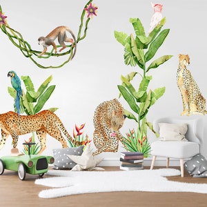 May include: A jungle-themed wall decal set featuring a monkey, a parrot, a pink flamingo, and two leopards. The decals are set against a white background with green banana leaves and pink flowers.