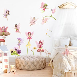 May include: A whimsical bedroom scene featuring fairy wall decals, a dollhouse, and a bed with a canopy. The fairies are depicted in various poses with colorful wings and dresses. Floral accents and mushroom decorations add to the fantasy theme.