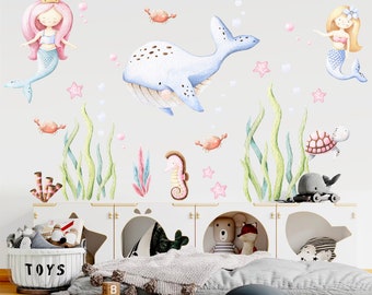 May include: A set of watercolor-style wall decals featuring a blue whale, two mermaids, a seahorse, a turtle, and seaweed. The decals are perfect for a nursery or child's room.