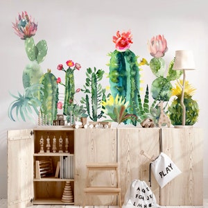 May include: A wall decal featuring a row of watercolour cactus plants with pink and red flowers. The decal is displayed on a wooden cabinet with two white canvas bags hanging on the cabinet doors. One bag says "PLAY" and the other has the letters of the alphabet printed on it.