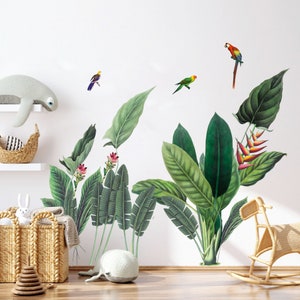May include: A tropical-themed wall decal featuring green leaves, pink flowers, and colourful parrots. The decal is shown on a white wall with a wicker basket and a stuffed animal on a shelf.