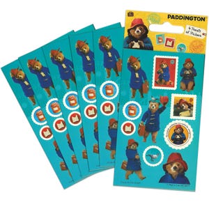 Puede incluir: Un conjunto de pegatinas de Paddington Bear sobre un fondo turquesa. Las pegatinas presentan a Paddington con un abrigo azul y un sombrero rojo, junto con imágenes de sándwiches de mermelada y sellos. El paquete dice "PADDINGTON" y "6 Sheets of Stickers."