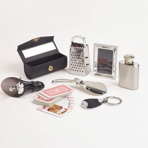 May include: An assortment of small items including a black leather glasses case, a stainless steel grater, a silver picture frame, a silver flask, a bottle stopper, a deck of playing cards, a shoe horn, and a keychain.